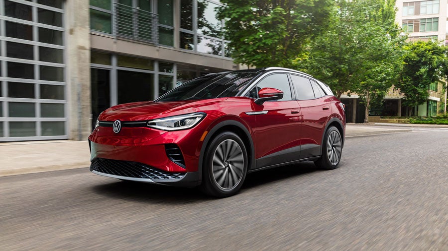 A ¾ front shot at street-level of an ID.4 SUV shown in Aurora Red Metallic, driving on a treelined, modern city street.